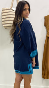 Woman wearing a navy dress with blue trim standing against a white wall.