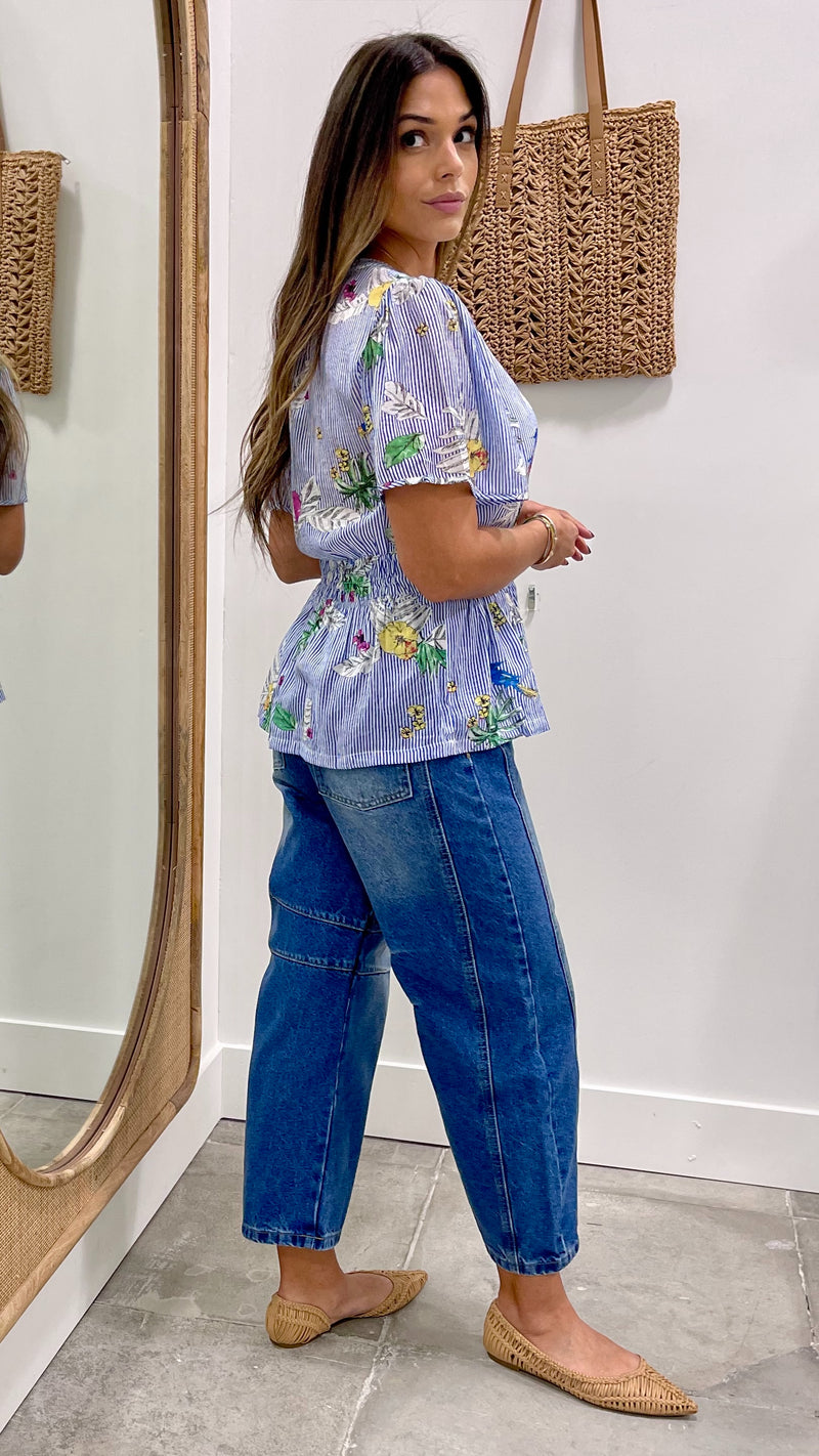 Woman wearing a floral blouse and blue jeans standing in front of a mirror.